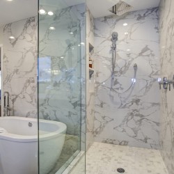 White and gray calcutta marble bathroom design with custom soaking tub and glass walk in shower.